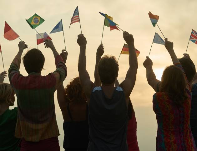 Concept of international friendship. People with different flags. Morning sky background.